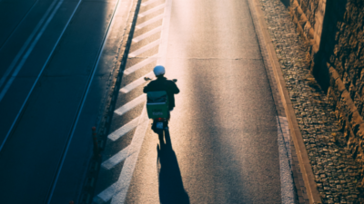 Man sieht eine*n Lieferant*in eines Online-Lieferdienst für Essen auf einem Motorroller. Das Bild steht sinnbildlich für die Arbeitenden in der Gig Economy in Kenia. You see a delivery person from an online food delivery service on a scooter. The image is emblematic of the workers in the gig economy in Kenya.