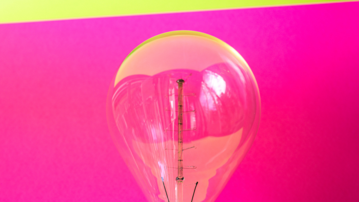 You can see a transparent light bulb in front of a pink background. It symbolizes new ideas for the field women in tech.