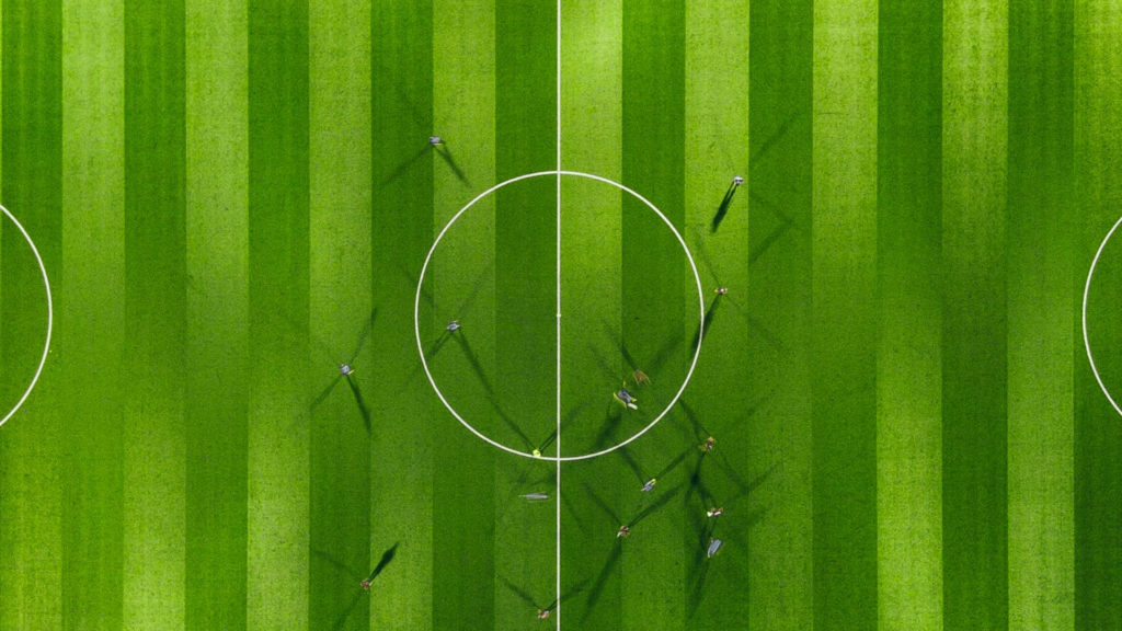 Das Bild zeigt ein Fußballfeld von oben. Die Spieler sind nur als Schatten zu erkennen, was den Human in the Loop repräsentieren soll.