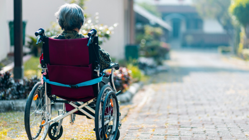 An older woman in a wheelchair sitting alone. This reflects the urgent need to combat loneliness through digital tools and community-based, inclusive care facilities.