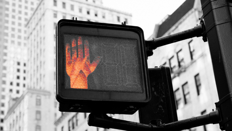 A close-up of a red pedestrian “stop” signal, symbolising public resistance and protest. The image evokes the growing global pushback against artificial intelligence systems and the demand to pause, question, and regulate their unchecked development.