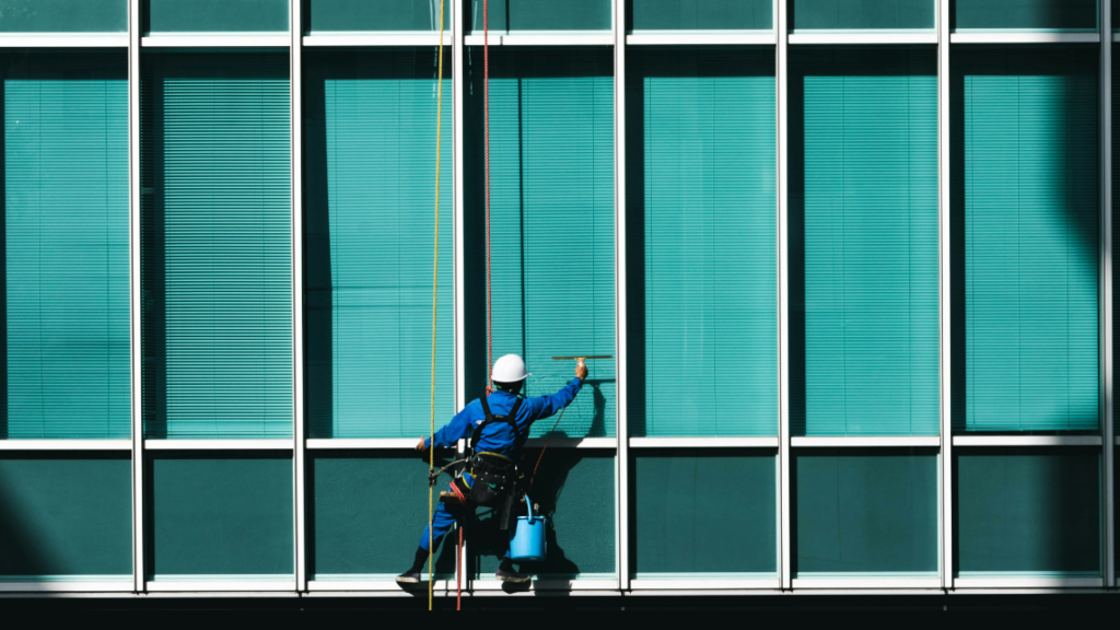 Das Foto zeigt einen Arbeiter, der eine blaue Glasfassade reinigt. Es steht symbolisch für Transparenz und das Hinterfragen von Annahmen über Desinformation.