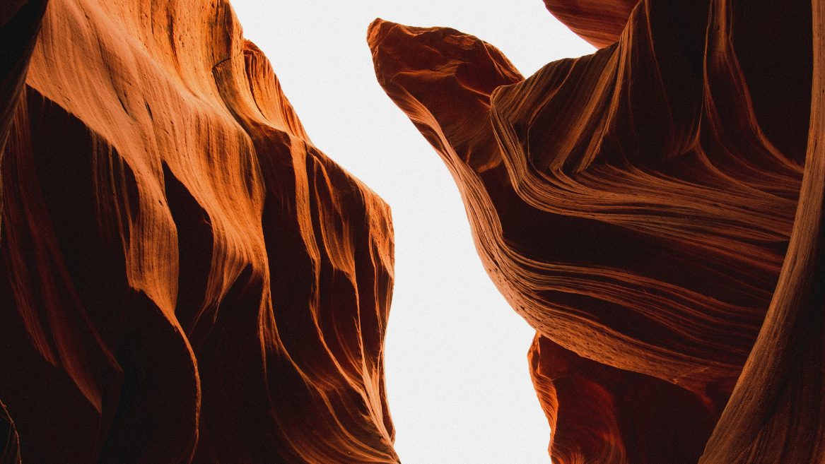 Deutsch: Blick nach oben zwischen hohen, geschwungenen Felswänden eines rot-orangefarbenen Canyons, dessen glatte, wellenförmige Formen von Licht und Schatten betont werden.