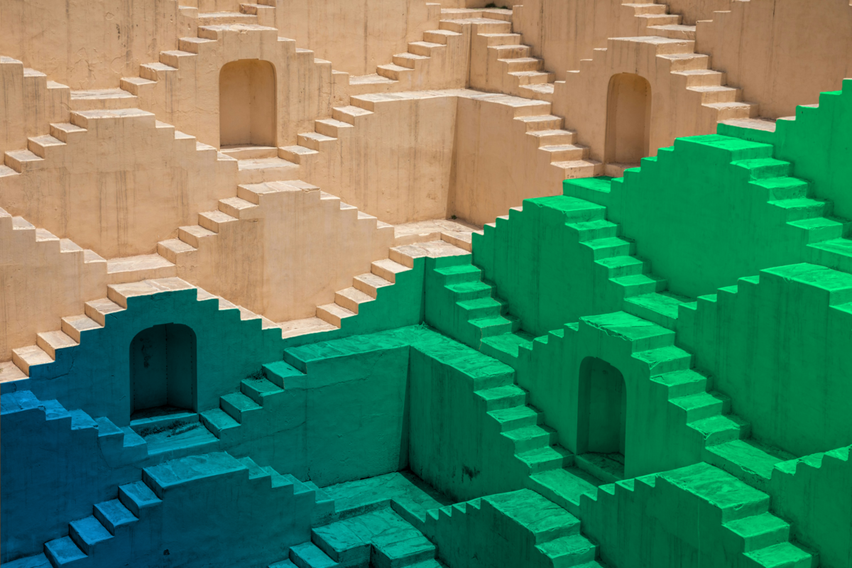 Eine verschachtelte Architektur aus Treppen und Torbögen leuchtet von Sandgelb über Blau bis Grün und symbolisiert die Hürden von KI-Unternehmer*innen und die Zukunft zur besseren Förderung.