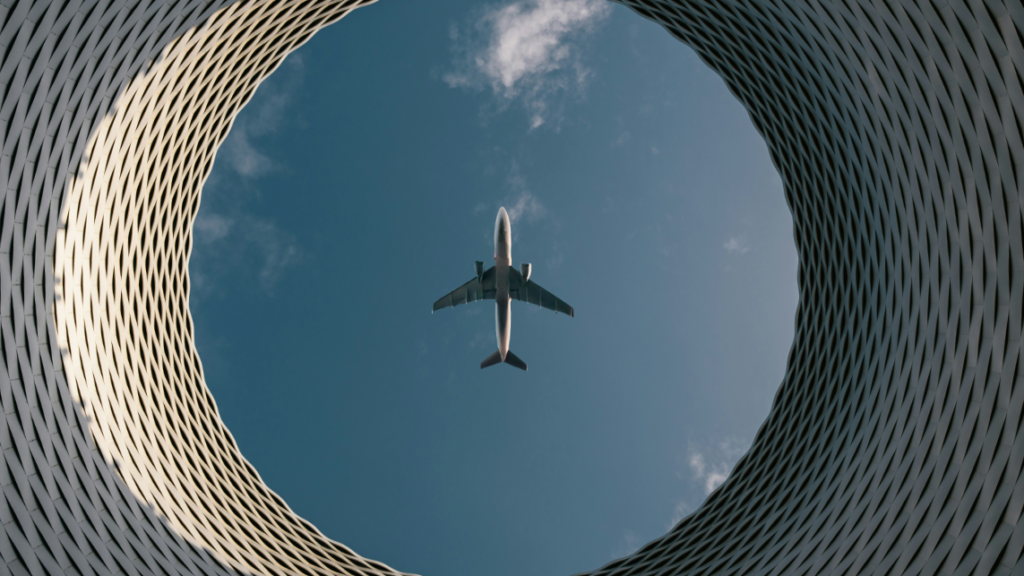 Das Foto zeigt ein Flugzeug von unten über einem runden Gebäude als Symbol für den Human in the Loop und Autopiloten in der Luftfahrt.
