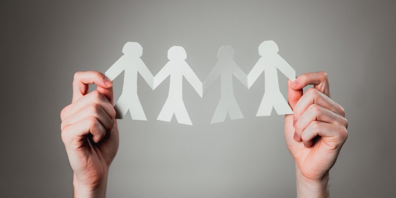 Two hands are holding a paper ribbon, that shows the outline of people holding hands