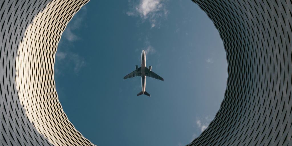 Luftfahrt Das Foto zeigt ein Flugzeug von unten über einem runden Gebäude als Symbol für den Human in the Loop und Autopiloten in der Luftfahrt.