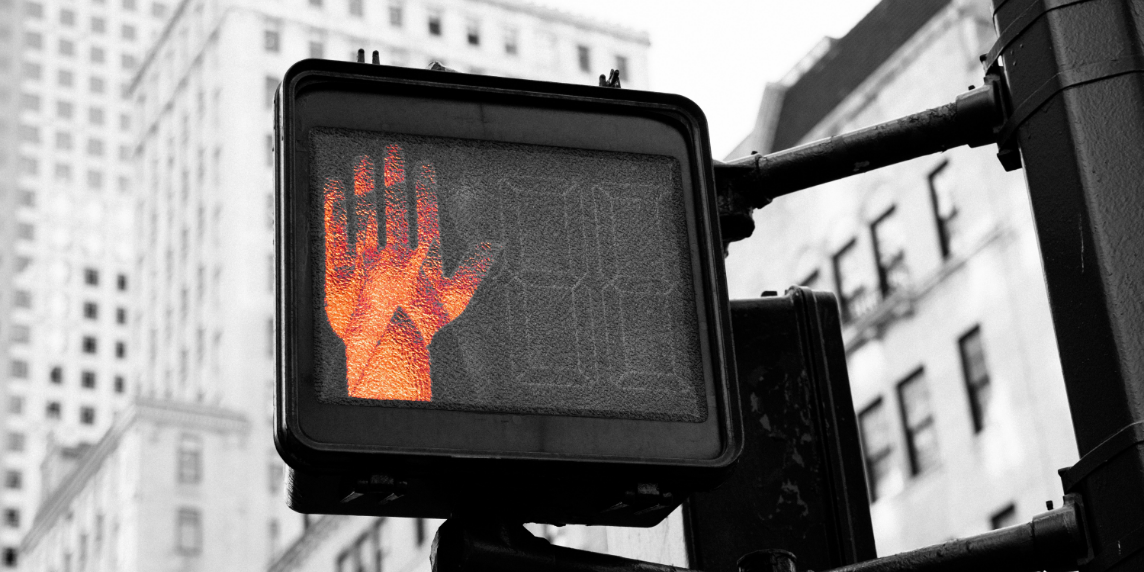 A close-up of a red pedestrian “stop” signal, symbolising public resistance and protest. The image evokes the growing global pushback against artificial intelligence systems and the demand to pause, question, and regulate their unchecked development.