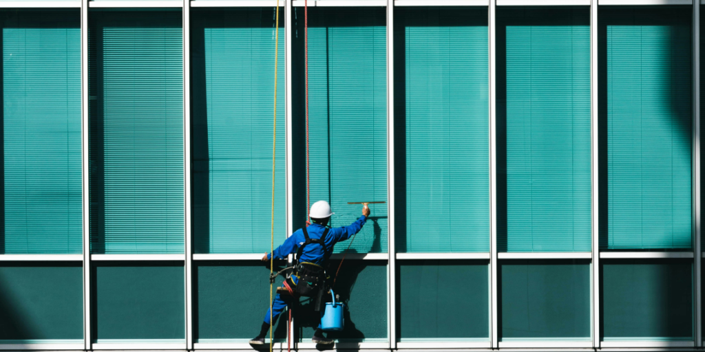 Das Foto zeigt einen Arbeiter, der eine blaue Glasfassade reinigt. Es steht symbolisch für Transparenz und das Hinterfragen von Annahmen über Desinformation.