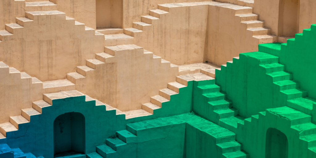 Titelbild_OpenCallAlica Eine verschachtelte Architektur aus Treppen und Torbögen leuchtet von Sandgelb über Blau bis Grün und symbolisiert die Hürden von KI-Unternehmer*innen und die Zukunft zur besseren Förderung.
