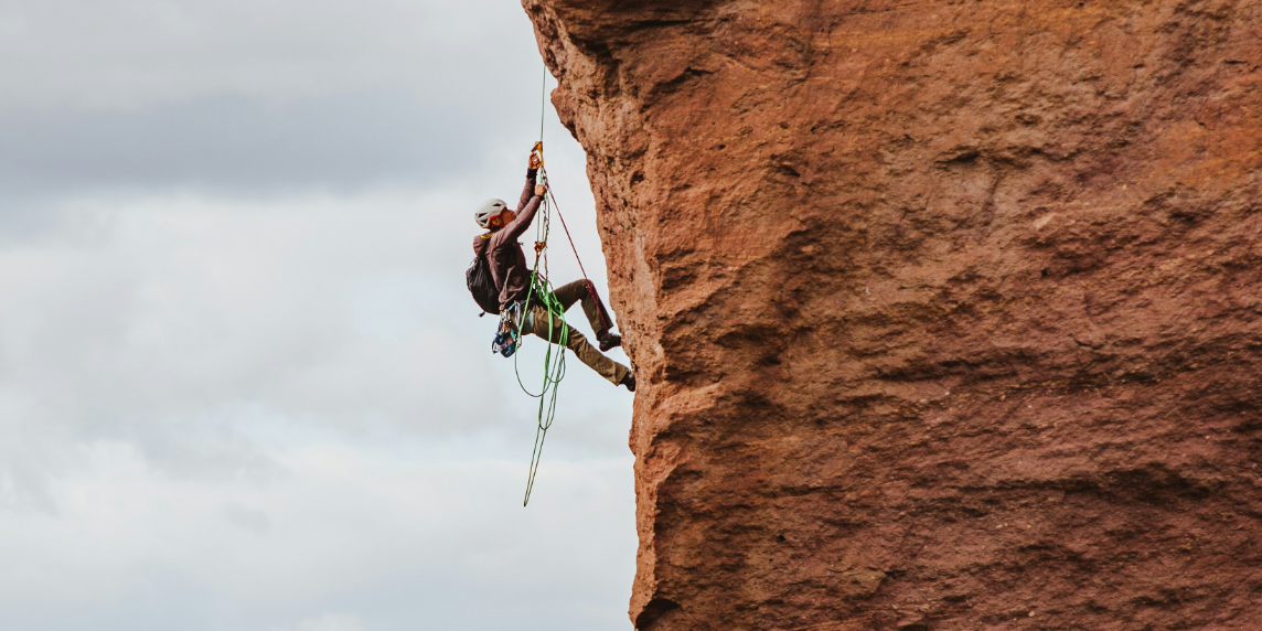 Titelbild_Paola – 3 A person climbing a steep rock face, symbolising the effort AI observatories make to scrutinise and challenge the structures of algorithmic power.