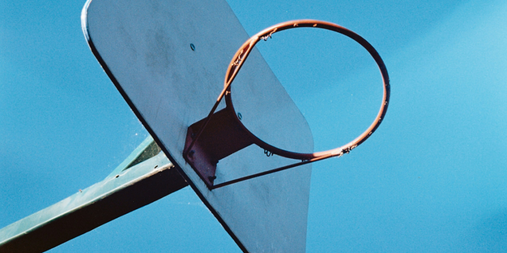 Titelbild_Sonja – 12 Das Bild zeigt den orangenen Ring eines Basketballkorbs vor blauem Himmel, symbolisch für den Human in the Loop in der Kreditvergabe.