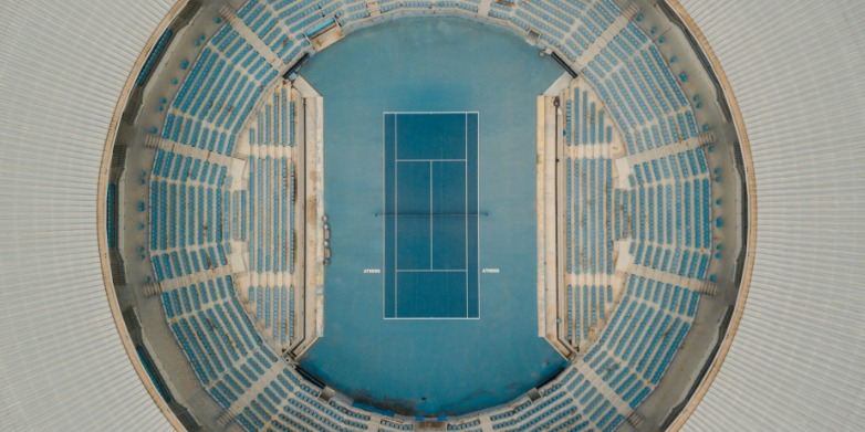 Zeichenfläche – 2 Eine Luftaufnahme eines großen Sportstadions mit blauen Sitzplätzen und einem weißen Spielfeld. Das Bild symbolisiert globale Zusammenarbeit und unterschiedliche Perspektiven, passend zum Thema des Aufrufs zur Einreichung von Beiträgen zur Mensch-Maschine-Interaktion in der Content-Moderation.
